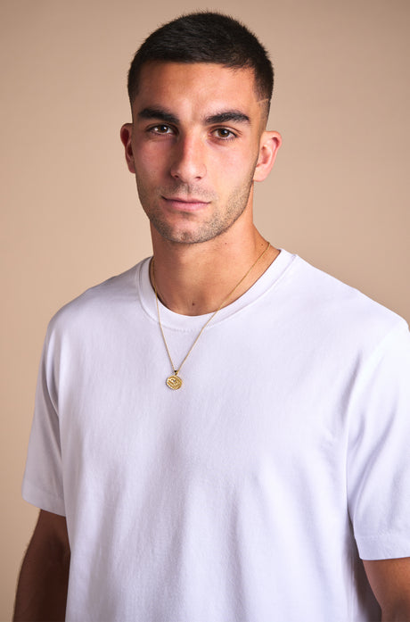 Gold necklace with a pendant in the shape of Spotify Camp Nou stadium, featuring a central sparkling gemstone, displayed between two textured rocks.