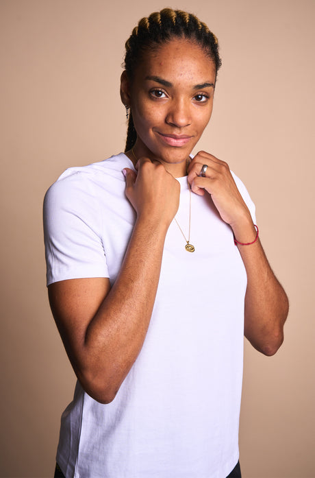 Gold necklace with a pendant in the shape of Spotify Camp Nou stadium, featuring a central sparkling gemstone, displayed between two textured rocks.