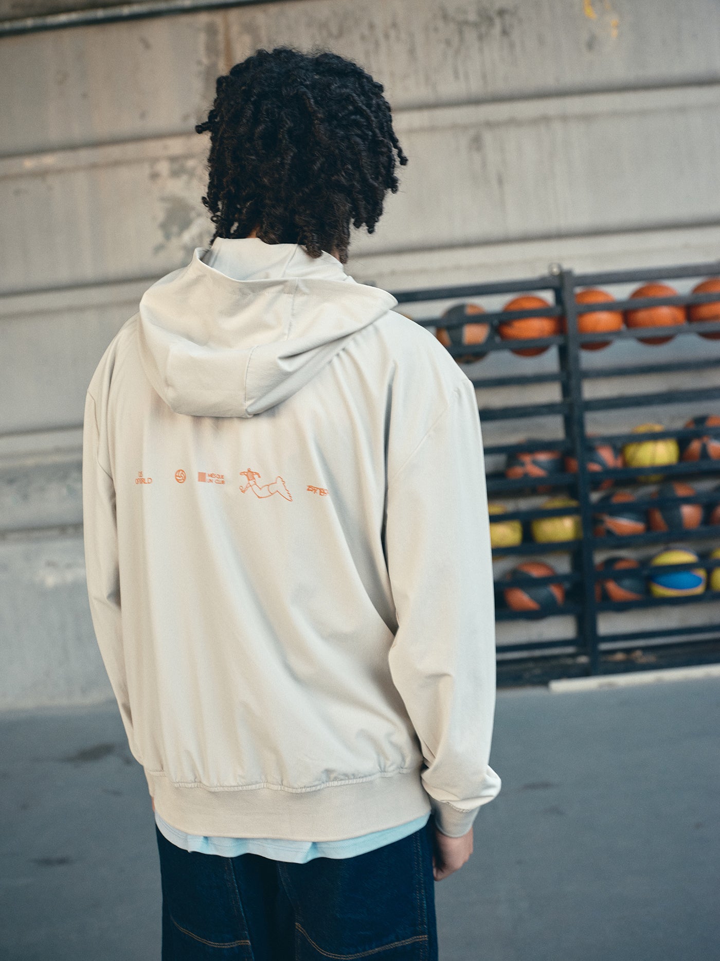 Beige FC Barcelona hooded jacket with minimalist orange graphic icons and text printed across the upper back.