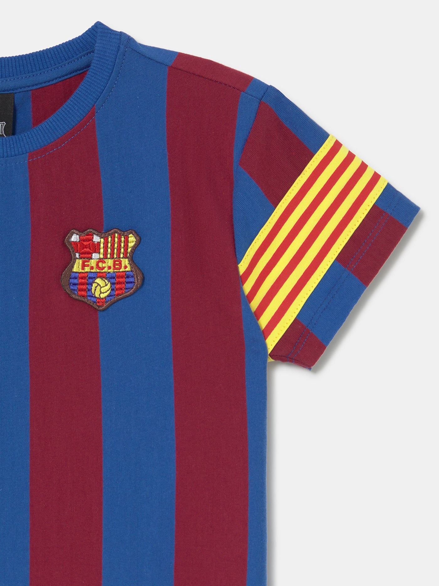FC Barcelona kids’ T-shirt with blue and maroon vertical stripes, embroidered club crest on the chest, and yellow-red striped armband detail on the sleeve