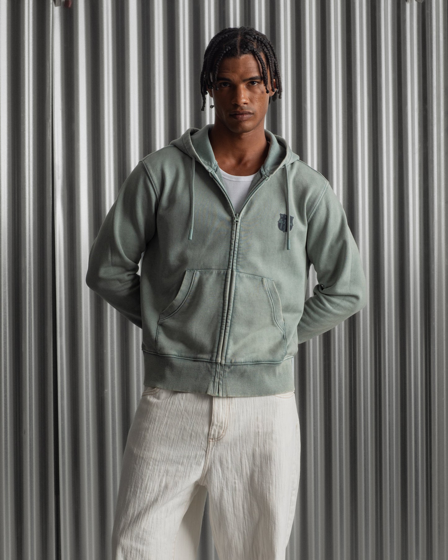 light green FC Barcelona zip-up hoodie with the club’s crest in dark print on the chest, standing against a metallic background.