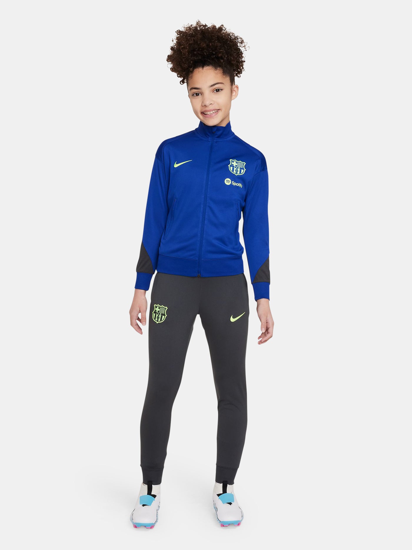 Women's FC Barcelona tracksuit featuring a blue zip-up jacket with neon green Nike and club logos, and dark grey pants with matching neon green details.