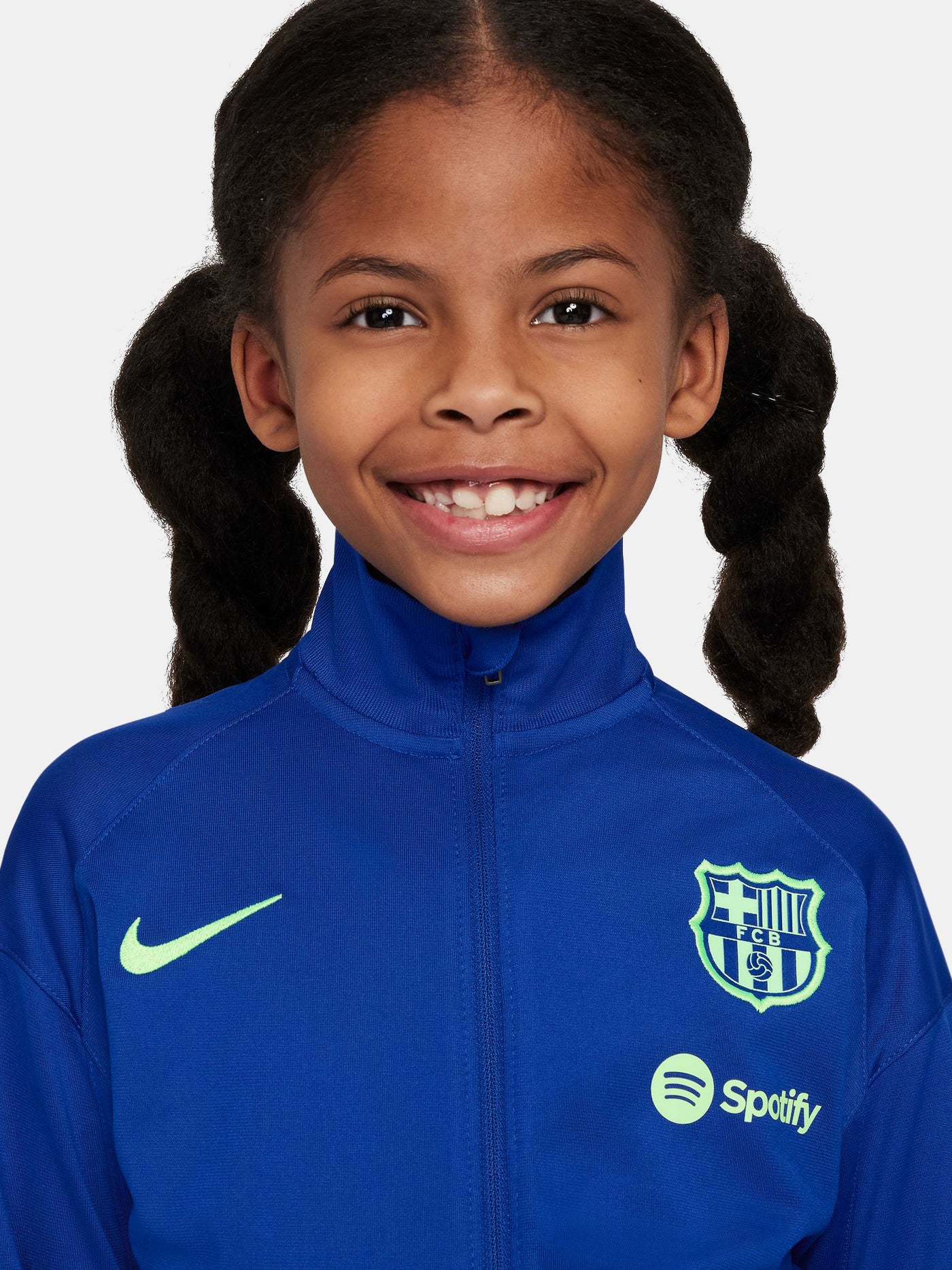 Kids' FC Barcelona tracksuit with blue jacket and black pants, featuring neon green crest and Nike logos.