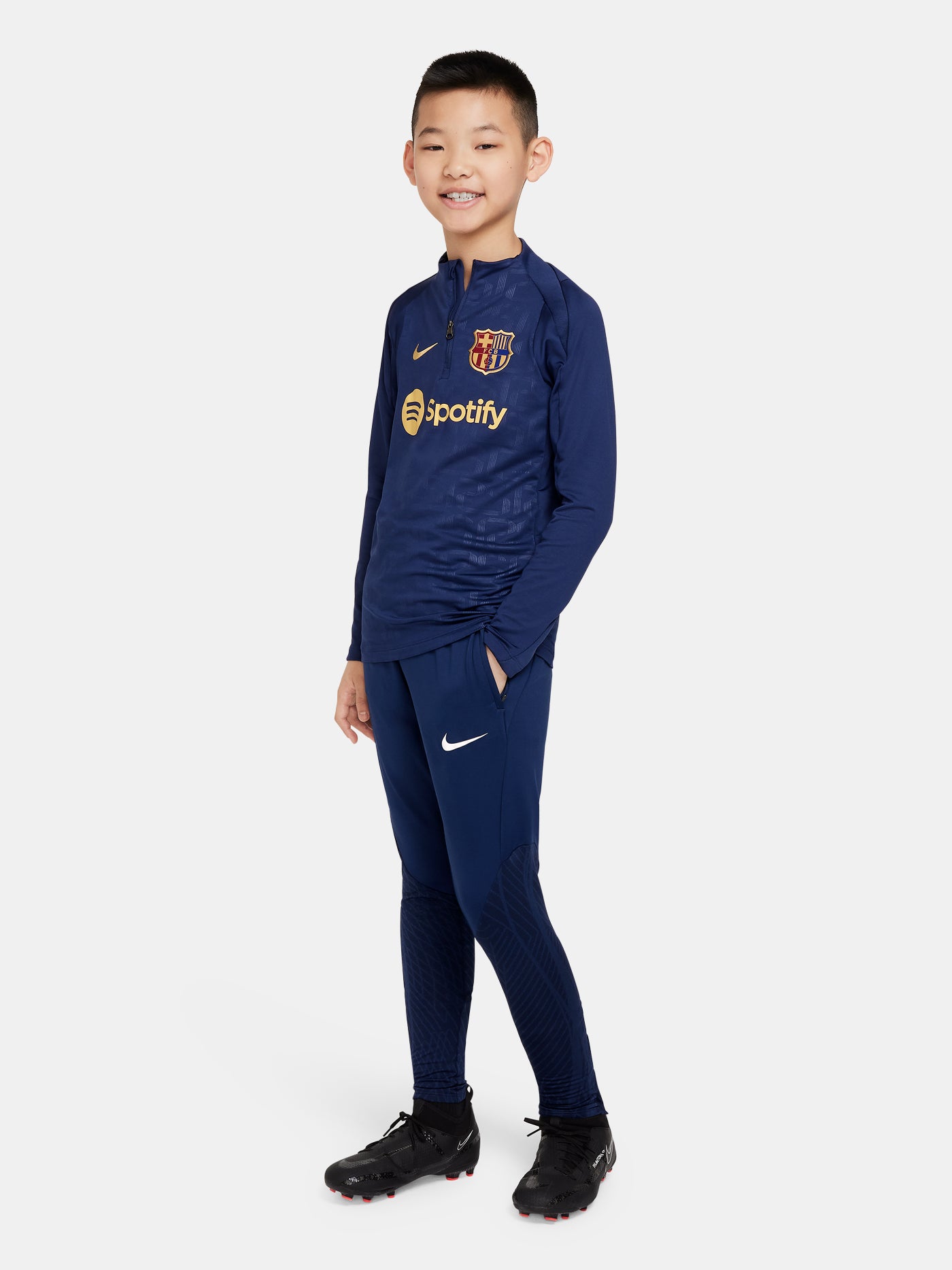 Youth FC Barcelona long-sleeve training top in navy blue with subtle embossed patterns, featuring gold Nike, Spotify, and club logos.