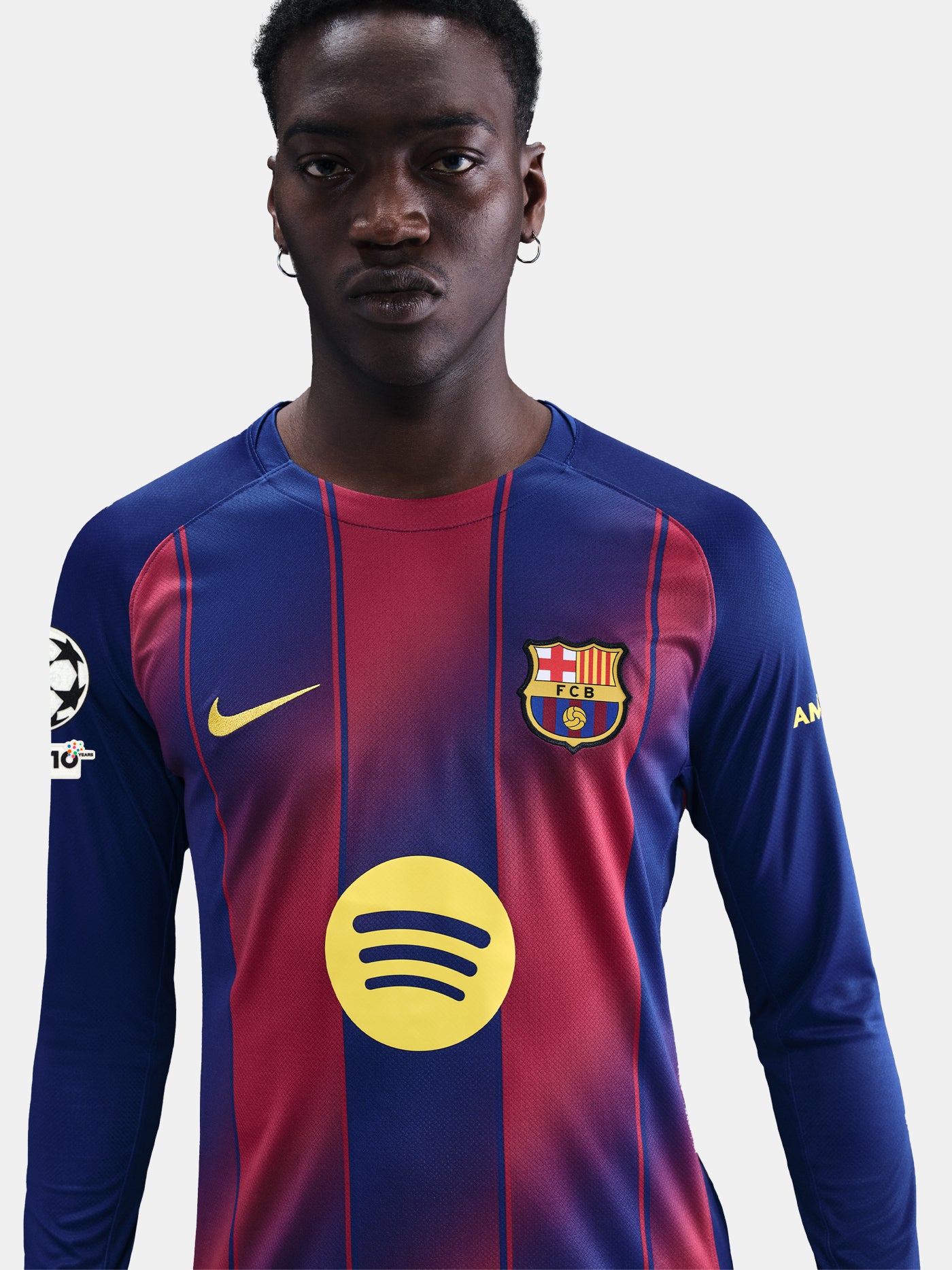 Portrait of a male model in FC Barcelona's long-sleeve home jersey, standing confidently and facing forward. The shirt features red and blue stripes, the Spotify sponsor logo, and UEFA Champions League and Nike branding.