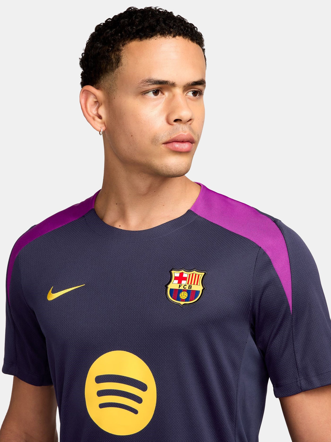 FC Barcelona navy training shirt with purple shoulder accents, yellow Nike logo, club crest, and Spotify sponsor, paired with gray shorts featuring a coral Nike logo.