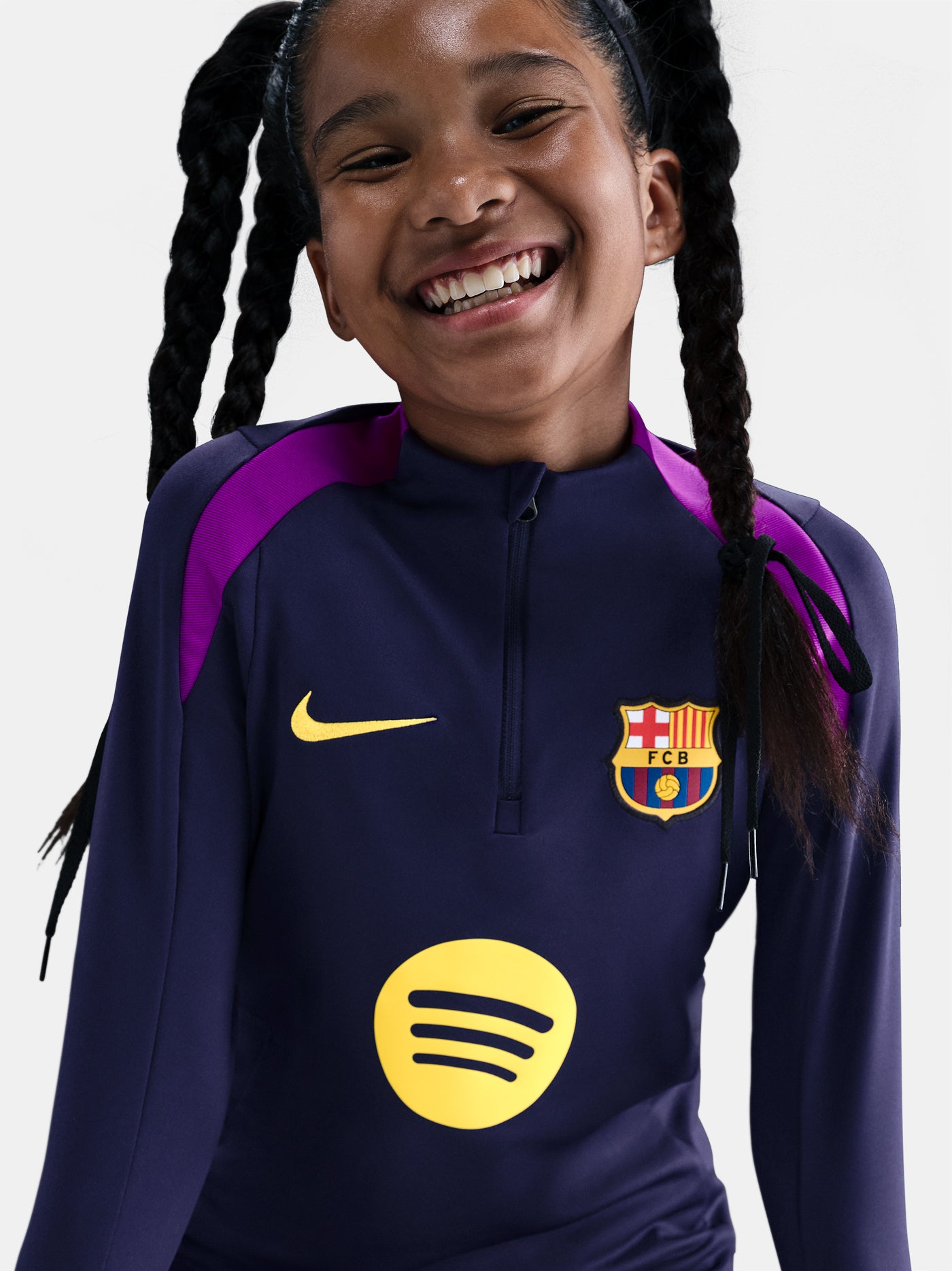 FC Barcelona long-sleeve training top for kids, in deep navy with vibrant magenta shoulder accents. Features include a half-zip design, yellow Nike swoosh, the Spotify sponsor logo, and the club crest prominently displayed—designed for comfort and performance on the pitch.