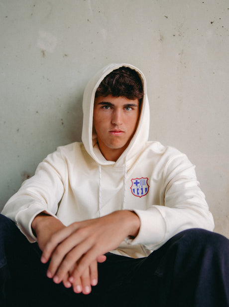 Back of a light hoodie featuring a vibrant FC Barcelona graphic design in blue, red, and white. The collage includes elements like a trophy, football, “GOAL,” “DIA DE PARTIT,” “1899,” and the Barça crest. Surrounding the design are phrases like “FC BARCELONA,” “TOTS UNITS FEM FORÇA,” “SENTIMENT BLAUGRANA,” and “MÉS QUE UN CLUB.”