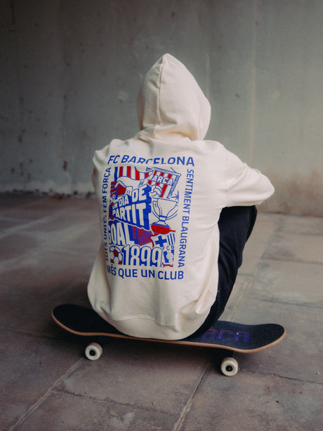 Back of a light hoodie featuring a vibrant FC Barcelona graphic design in blue, red, and white. The collage includes elements like a trophy, football, “GOAL,” “DIA DE PARTIT,” “1899,” and the Barça crest. Surrounding the design are phrases like “FC BARCELONA,” “TOTS UNITS FEM FORÇA,” “SENTIMENT BLAUGRANA,” and “MÉS QUE UN CLUB.”