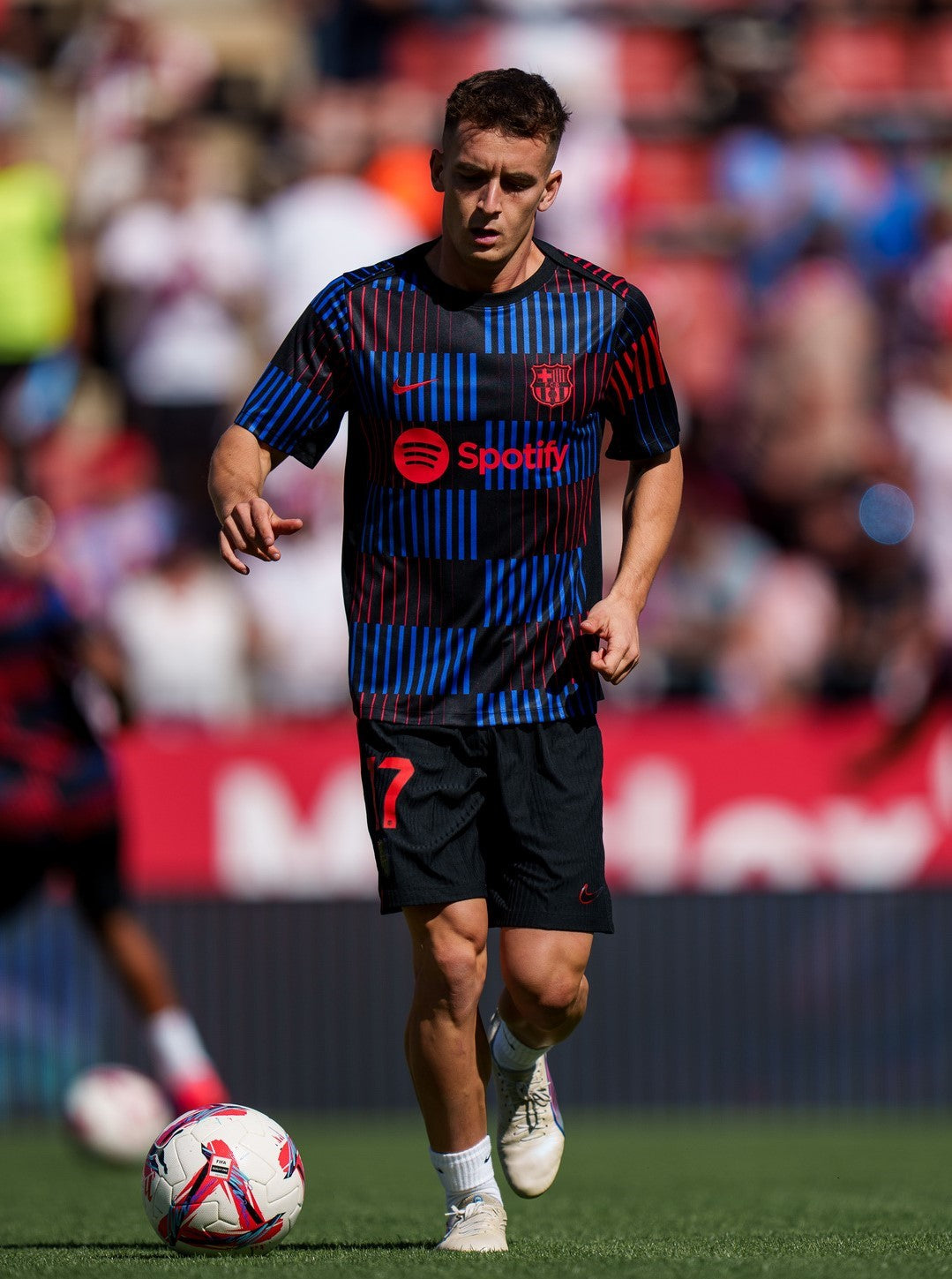 FC Barcelona warm-up shirt featuring a black base with a striking vertical stripe pattern in alternating red and blue. The shirt displays the red Spotify logo in the center, along with the Nike swoosh and FC Barcelona crest, also in red.