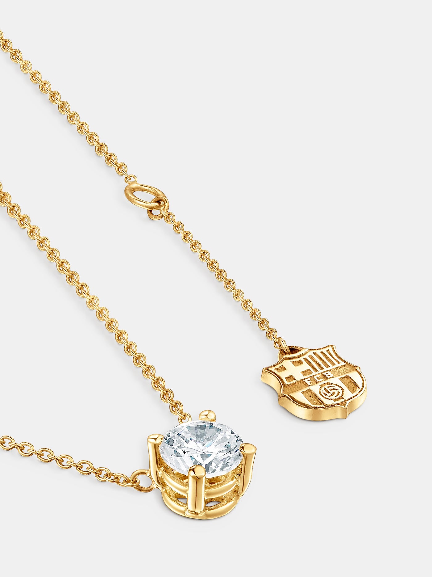 Elegant gold necklace featuring a central diamond-like stone and a small hanging FC Barcelona crest charm near the clasp.