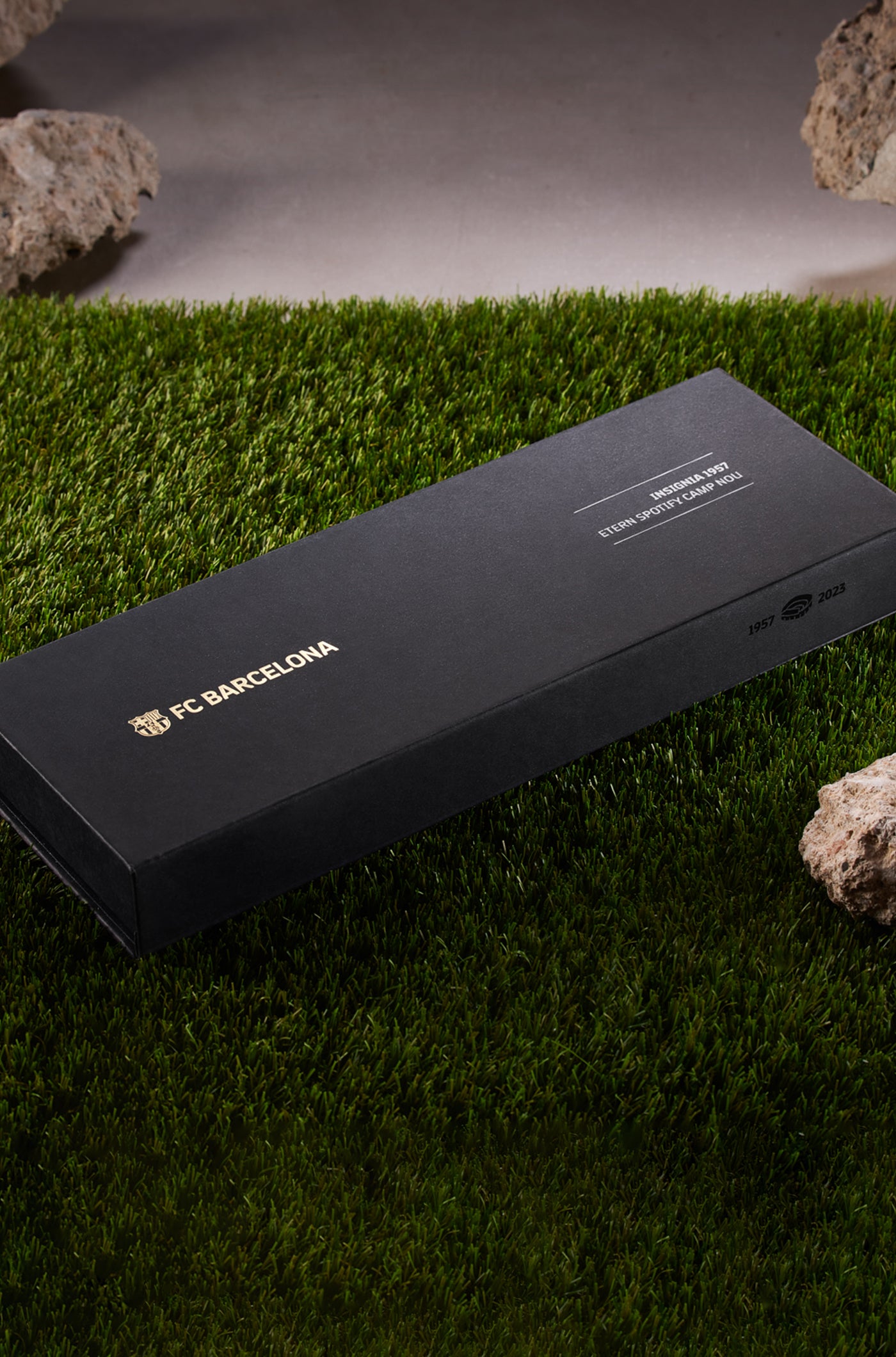 Black leather bracelet with red stitching and red inner lining, featuring a gold buckle shaped like the Spotify Camp Nou stadium in blue, red, and white, with a sparkling gemstone in the center.