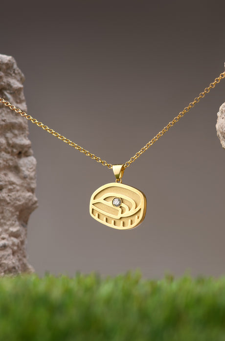 Gold necklace with a pendant in the shape of Spotify Camp Nou stadium, featuring a central sparkling gemstone, displayed between two textured rocks.