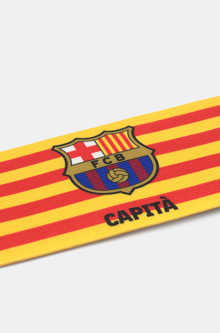 Yellow and red striped FC Barcelona captain's armband featuring the club crest and the word "CAPITÀ" printed in black.