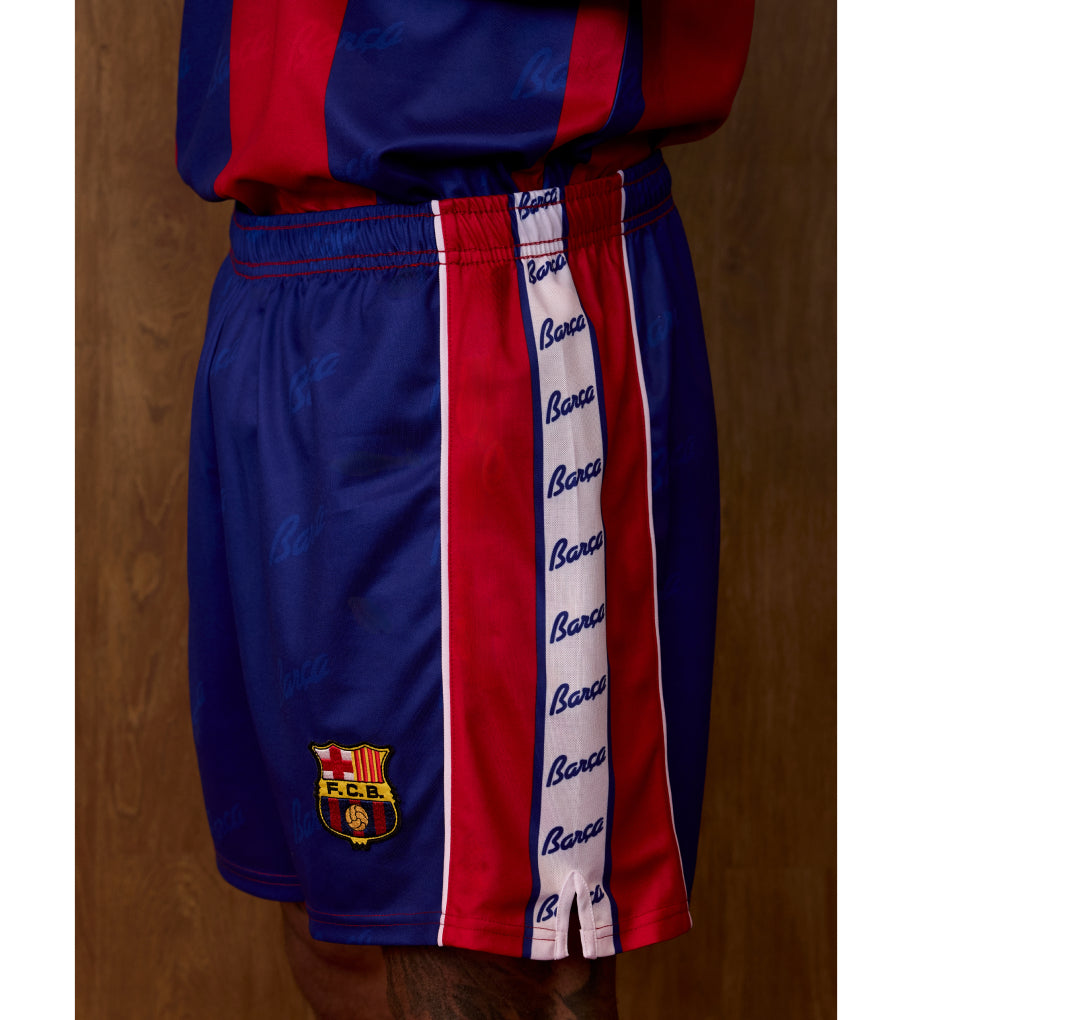 Side view of FC Barcelona shorts in blue and red with a vertical Barca script stripe and the club crest on the leg.
