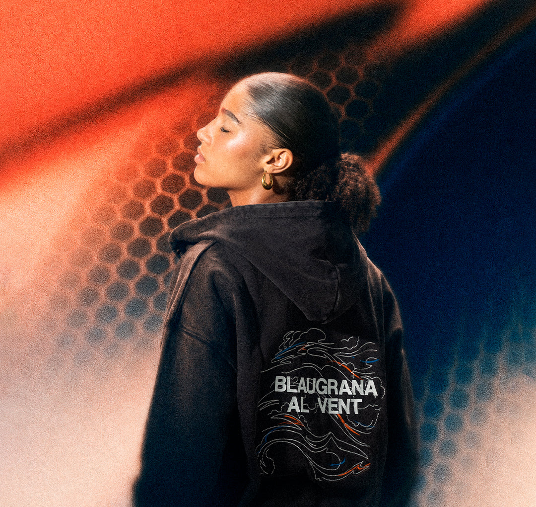 Vista trasera de una sudadera negra de FC Barcelona sobre una modelo, con “BLAUGRANA AL VENT” impreso en la espalda en blanco y gráficos de líneas de colores.