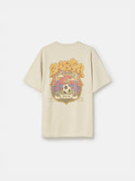 Beige FC Barcelona T-shirt featuring a vibrant vintage-style back print with the word "Barça" in large retro bubble letters. The graphic includes a football, flags, and stadium elements in bold colors within a shield-like frame. A ribbon below the design reads “Since 1899” and “Més que un club.”