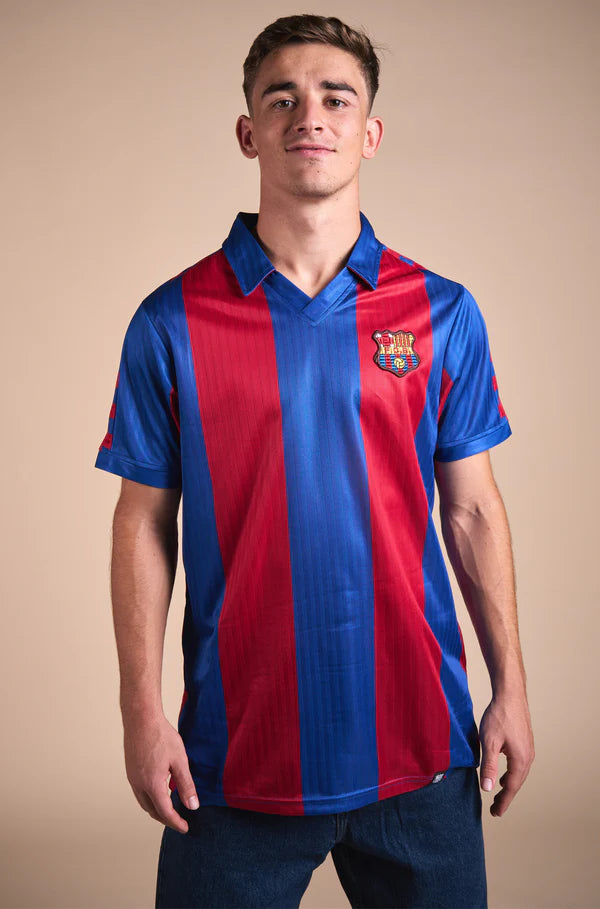 Man wearing a retro-style FC Barcelona jersey with wide vertical red and blue stripes, featuring the club's crest on the left chest and a classic V-neck collar design.