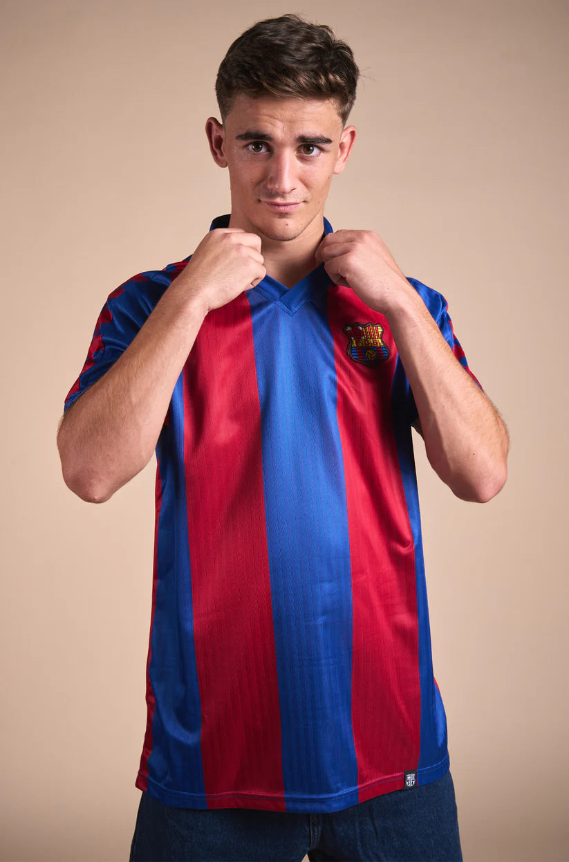 Man wearing a retro-style FC Barcelona jersey with wide vertical red and blue stripes, featuring the club's crest on the left chest and a classic V-neck collar design.
