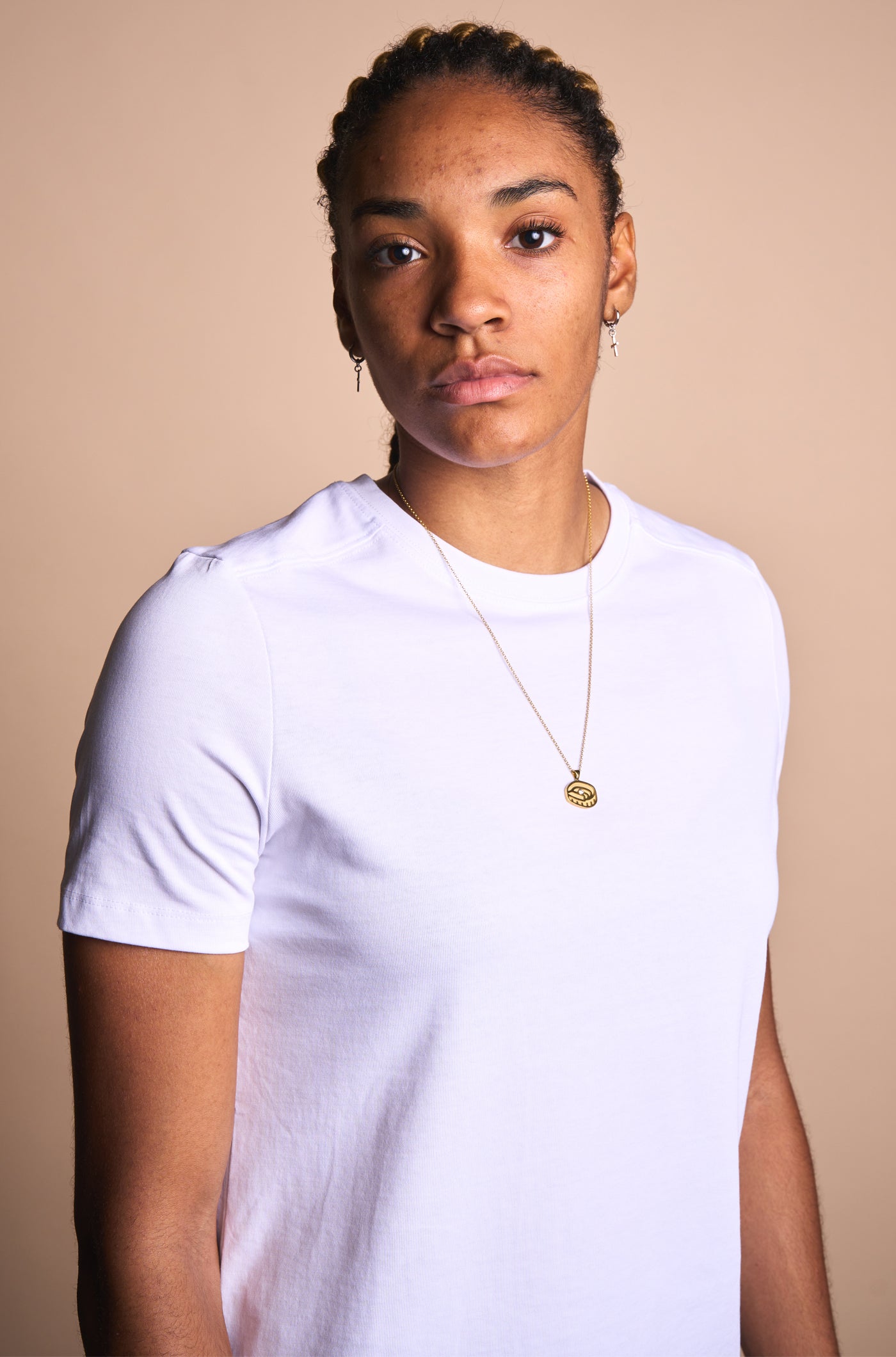 Gold necklace with a pendant in the shape of Spotify Camp Nou stadium, featuring a central sparkling gemstone, displayed between two textured rocks.