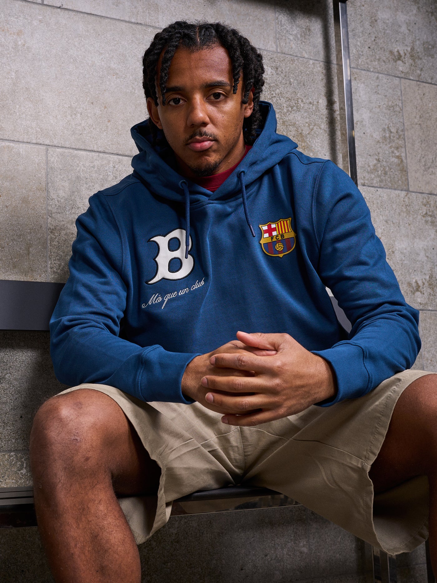 Man wearing a blue FC Barcelona hoodie, sitting with hands clasped. The hoodie features a white “B” on the left side with the phrase “Més que un club” below it, and the official FC Barcelona crest on the right side.









