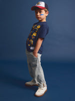 Child wearing a red and white cap and a navy FC Barcelona T-shirt with multiple illustrations of Cat Culer, the club’s mascot, in various poses.