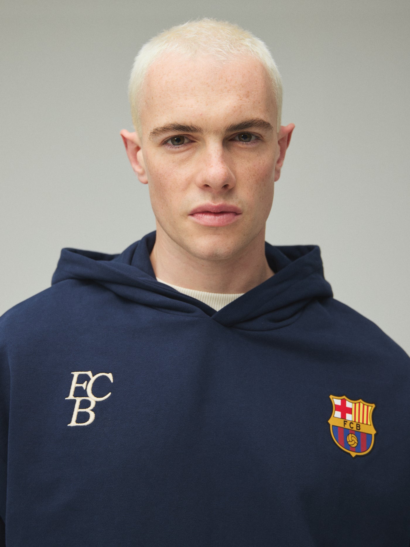 Model wearing a navy FC Barcelona hoodie with crest in a lifestyle ecommerce image.