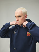 Model wearing a navy FC Barcelona hoodie with crest in a lifestyle ecommerce image.