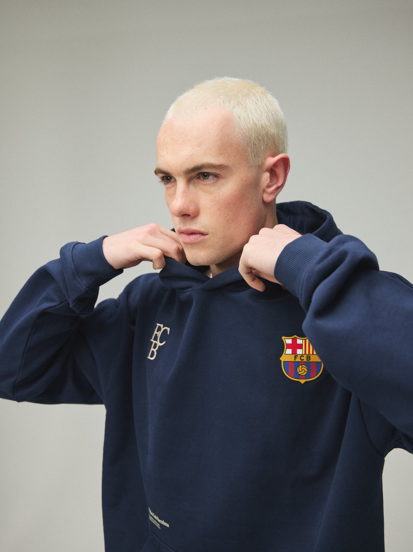 Model wearing a navy FC Barcelona hoodie with crest in a lifestyle ecommerce image.