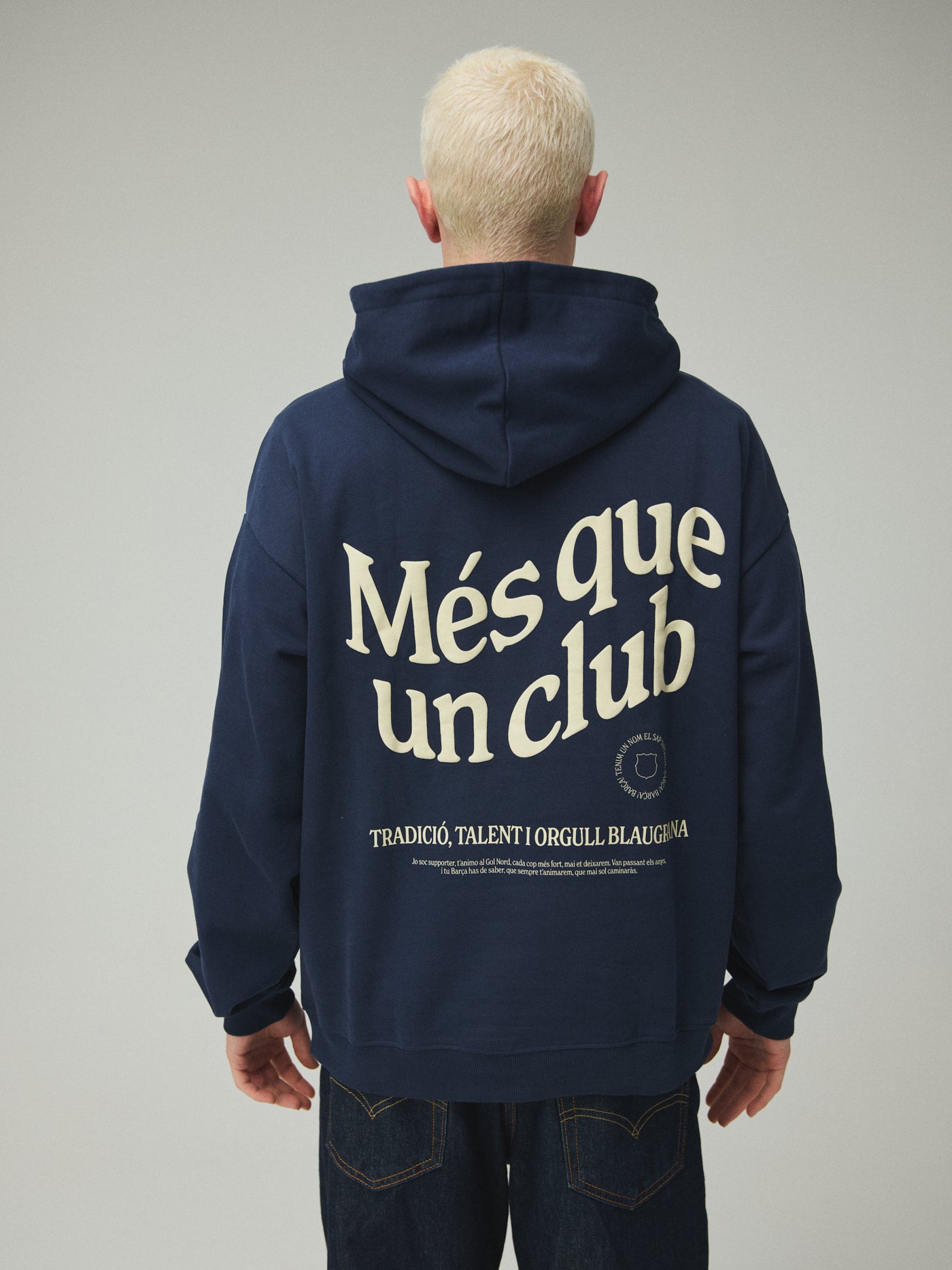 Model wearing a navy FC Barcelona hoodie with crest in a lifestyle ecommerce image.