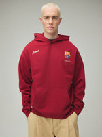 Model wearing a red FC Barcelona hoodie with crest in a lifestyle ecommerce image.