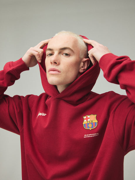 Model wearing a red FC Barcelona hoodie with crest in a lifestyle ecommerce image.