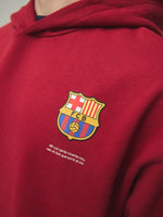 Model wearing a red FC Barcelona hoodie with crest in a lifestyle ecommerce image.