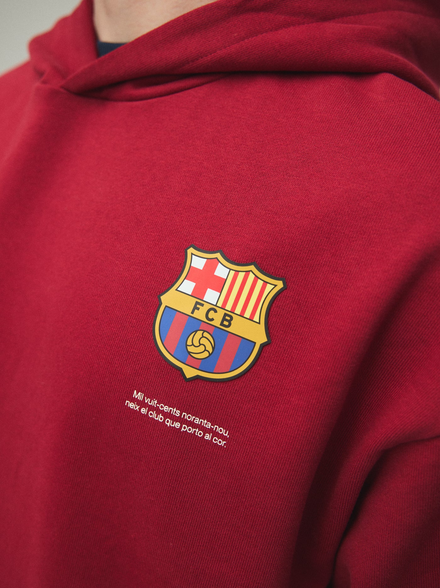 Model wearing a red FC Barcelona hoodie with crest in a lifestyle ecommerce image.