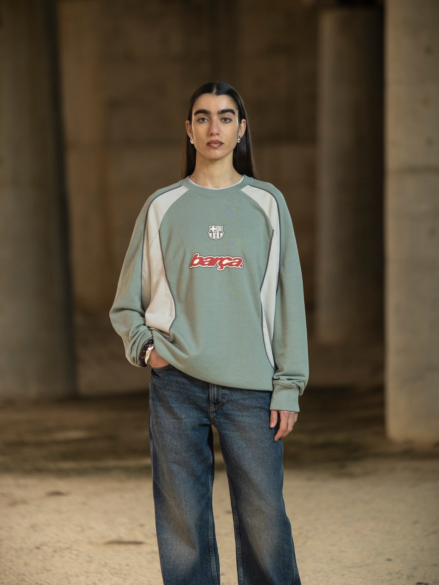 Person wearing a green and beige sweater with a logo, standing in a neutral setting.