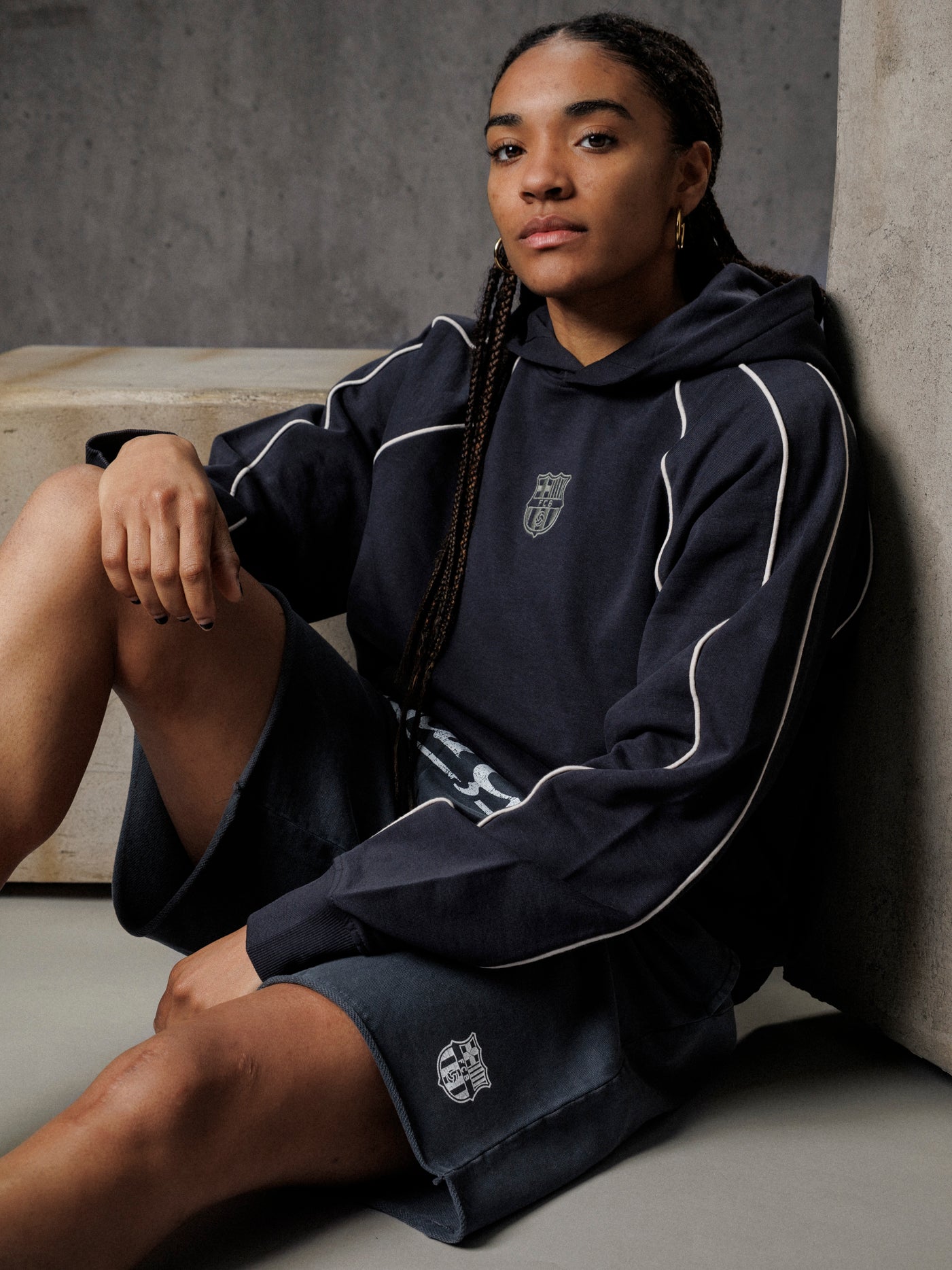 Person wearing a navy tracksuit with white accents sitting against a gray wall.