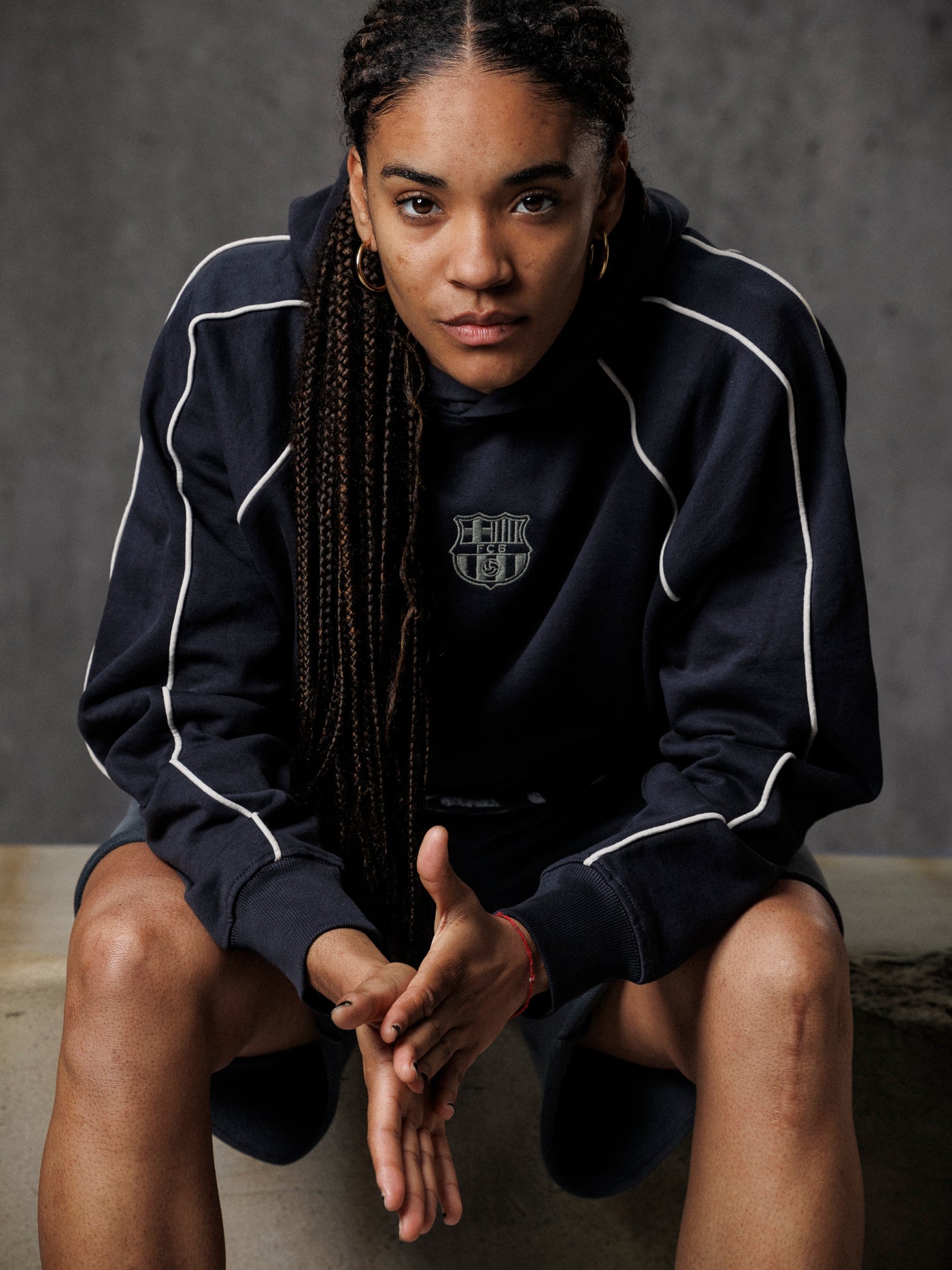 Person wearing a black tracksuit with white piping, sitting against a gray background