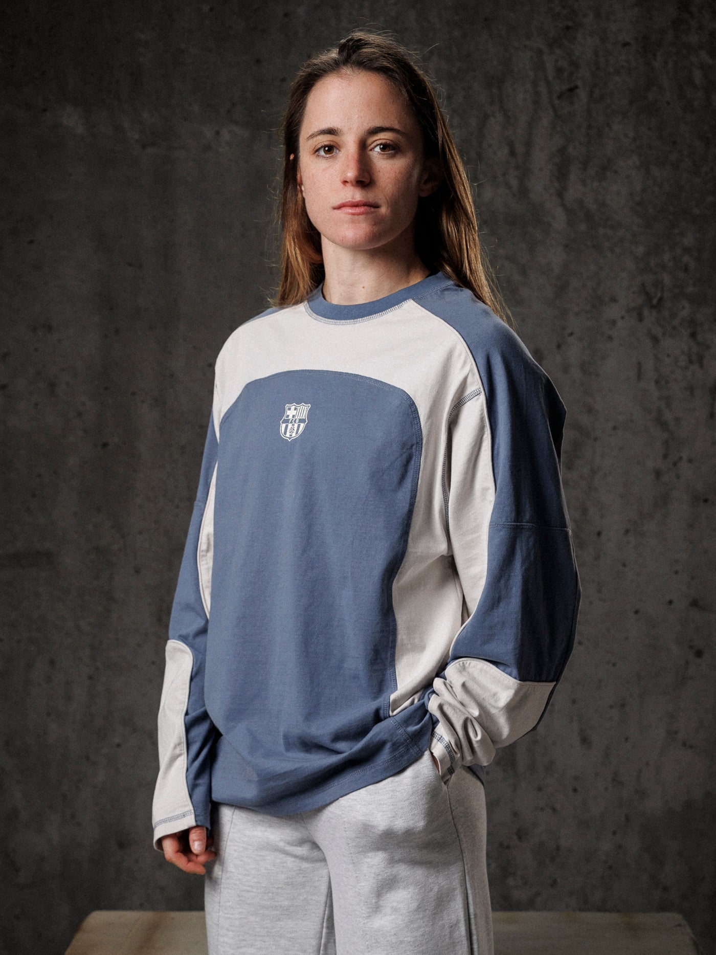 Person wearing a blue and beige long-sleeve shirt with a logo against a dark background