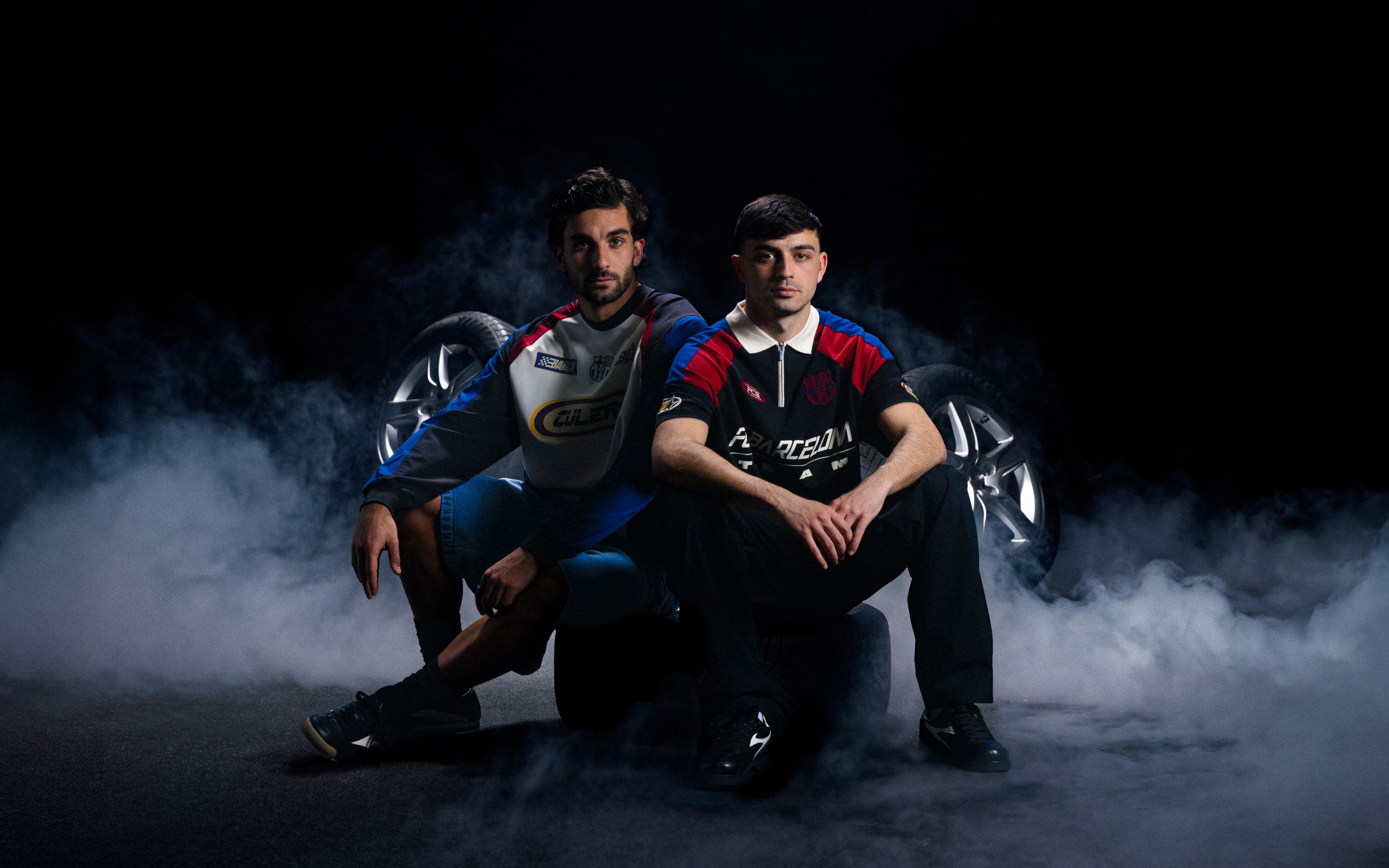 Two individuals in racing suits sitting on a dark background with smoke effects