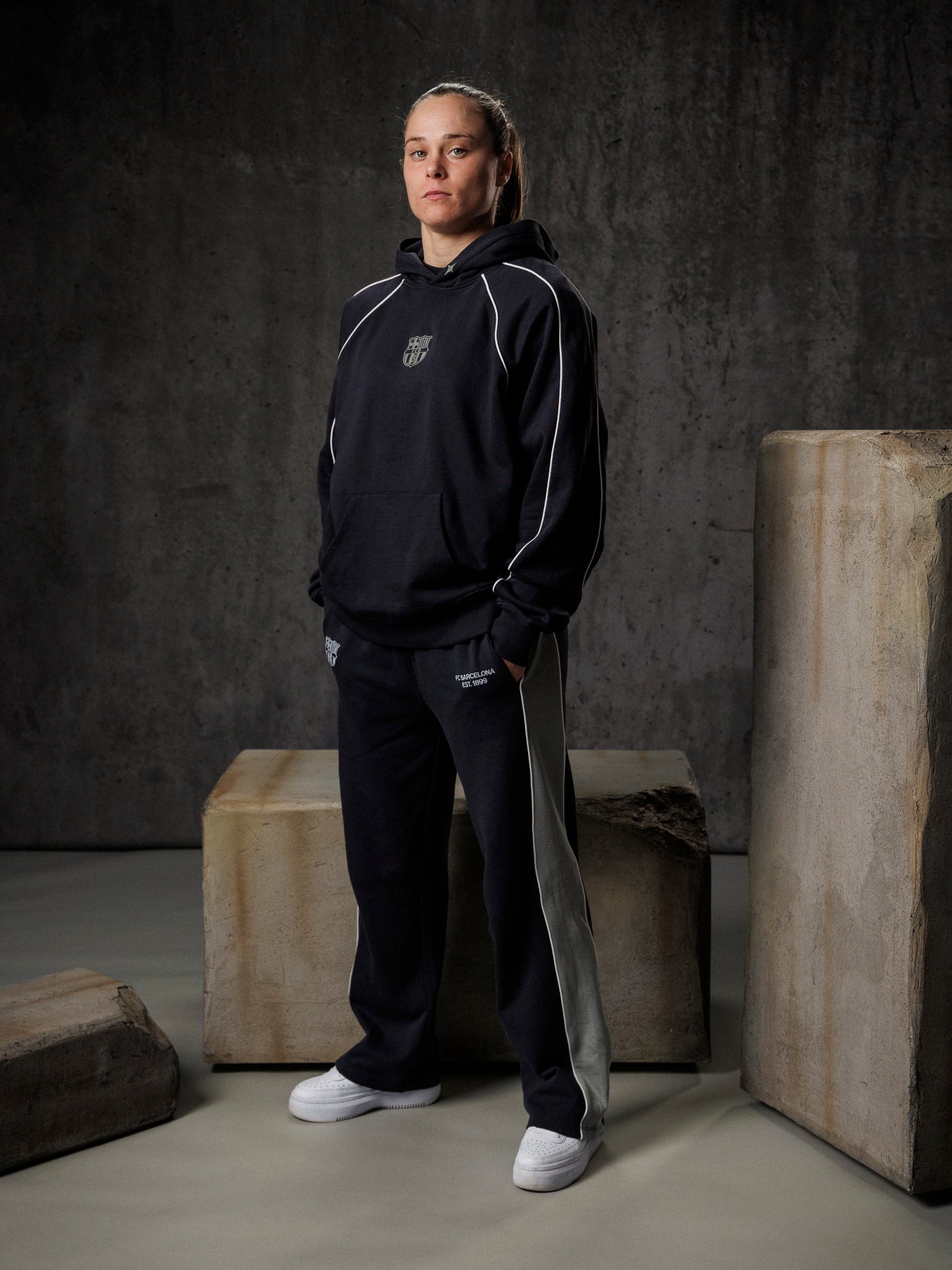 Person wearing a black tracksuit standing against a dark background