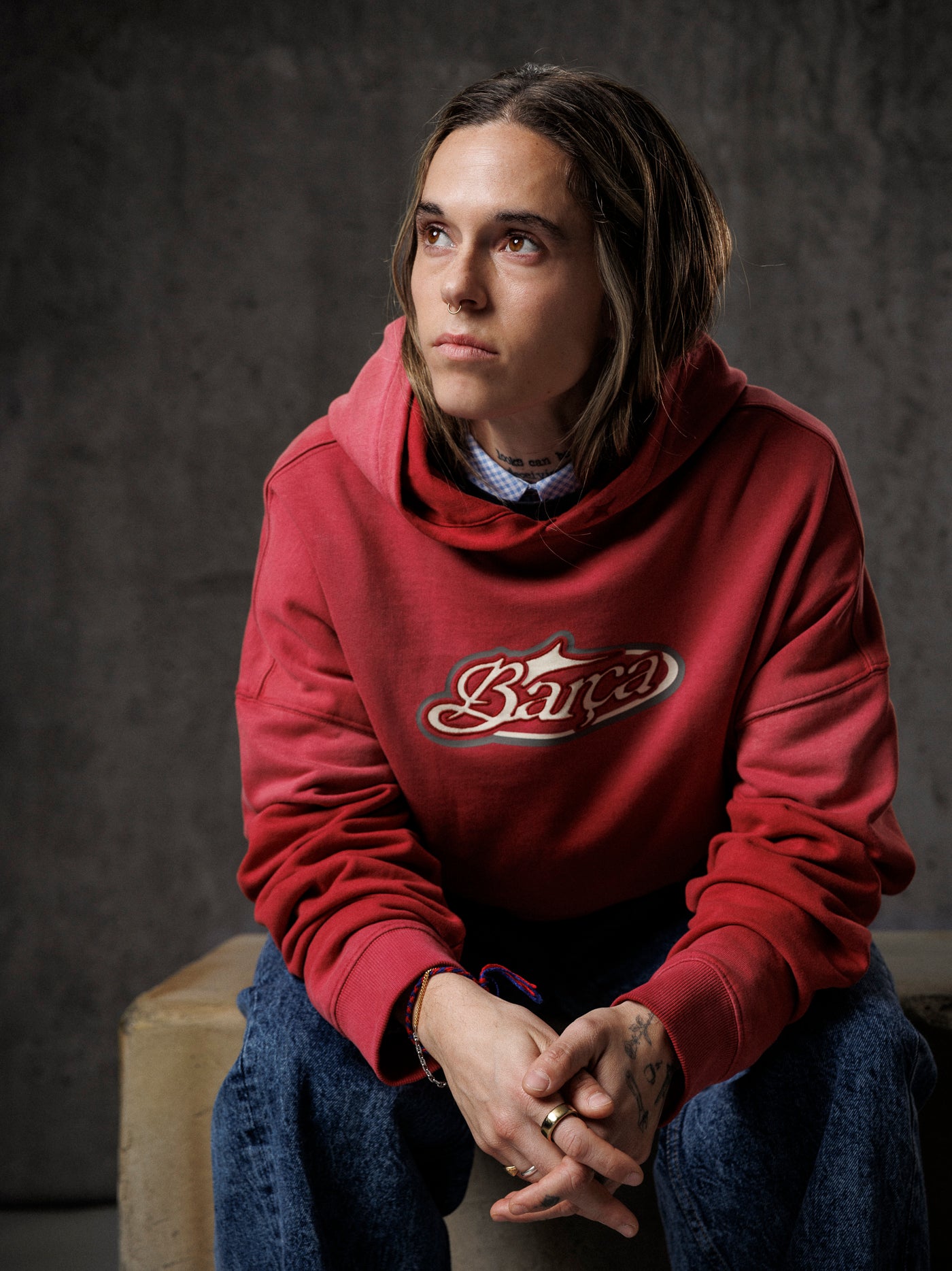 Person wearing a red hoodie with a logo, sitting on a bench against a dark background