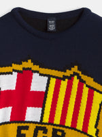 Close-up of a navy FC Barcelona knit sweater with a ribbed crew neck and a large woven club crest in red, yellow, white and black.