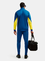 Person wearing a blue and yellow tracksuit holding a black bag on a white background