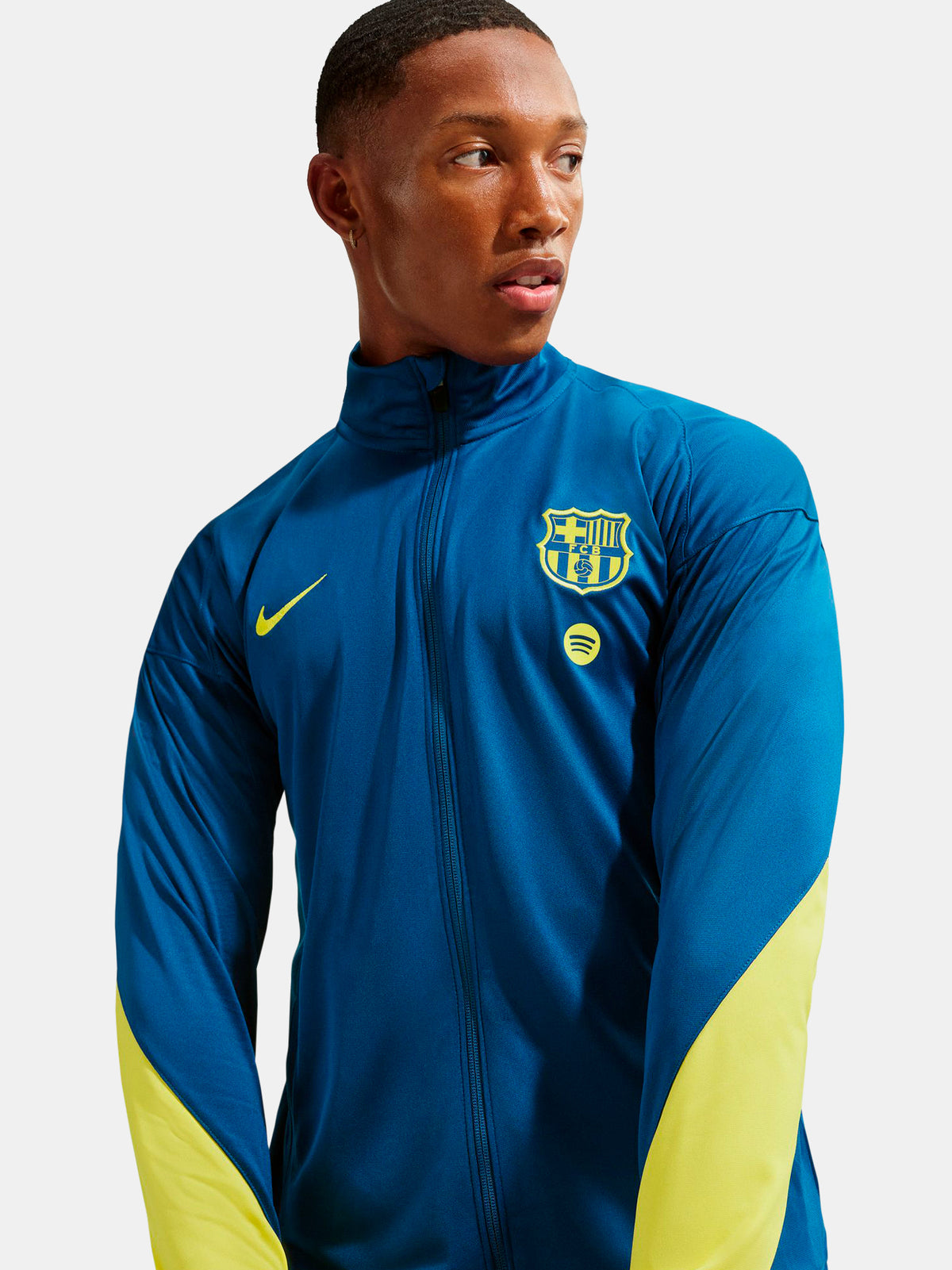 Person wearing a blue and yellow sports jacket with a logo on a light gray background