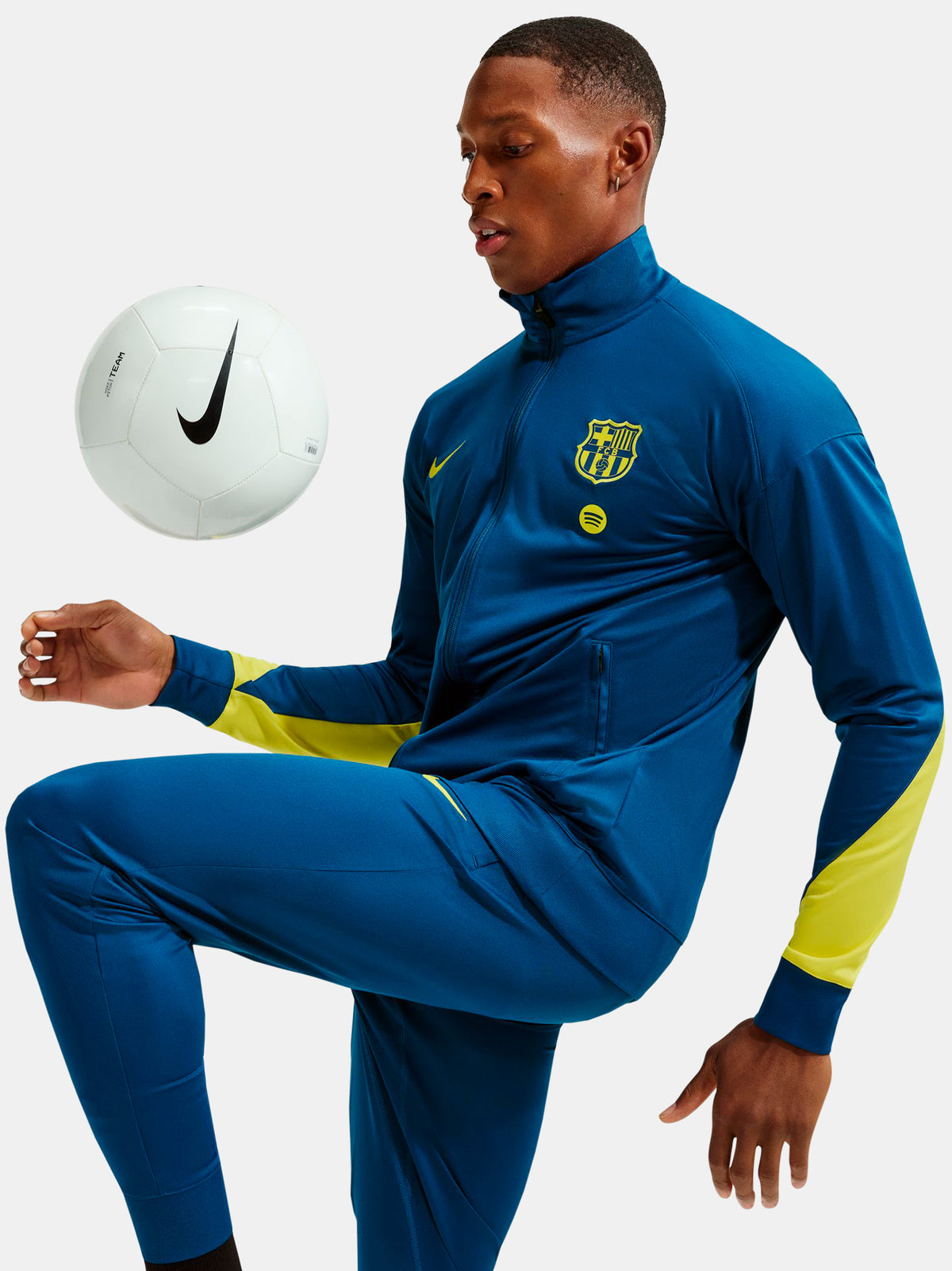 Person wearing a blue sports tracksuit with a Nike logo, kicking a white soccer ball.