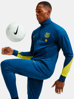 Person wearing a blue sports tracksuit with a Nike logo, kicking a white soccer ball.