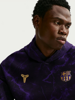 Modelo con sudadera morada con estampado marmolado, escudo del FC Barcelona y logo dorado en el pecho.