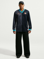 Vista frontal de un modelo con una prenda de manga larga azul marino oscuro de FC Barcelona con ribete turquesa, logo de Nike y escudo del club.
