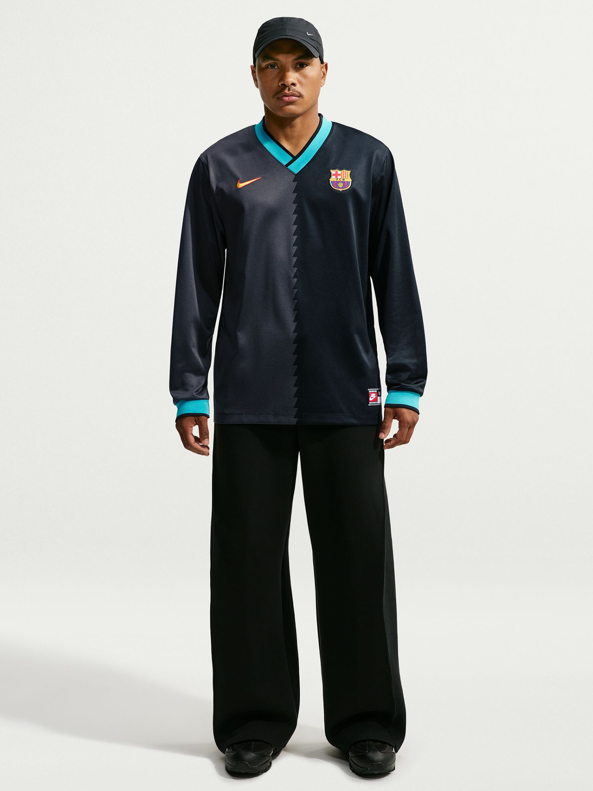 Vista frontal de un modelo con una prenda de manga larga azul marino oscuro de FC Barcelona con ribete turquesa, logo de Nike y escudo del club.