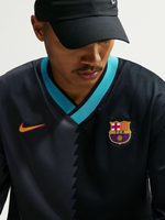 Modelo con la camiseta negra del FC Barcelona, cuello de pico turquesa, logo de Nike y escudo del club en el pecho.
